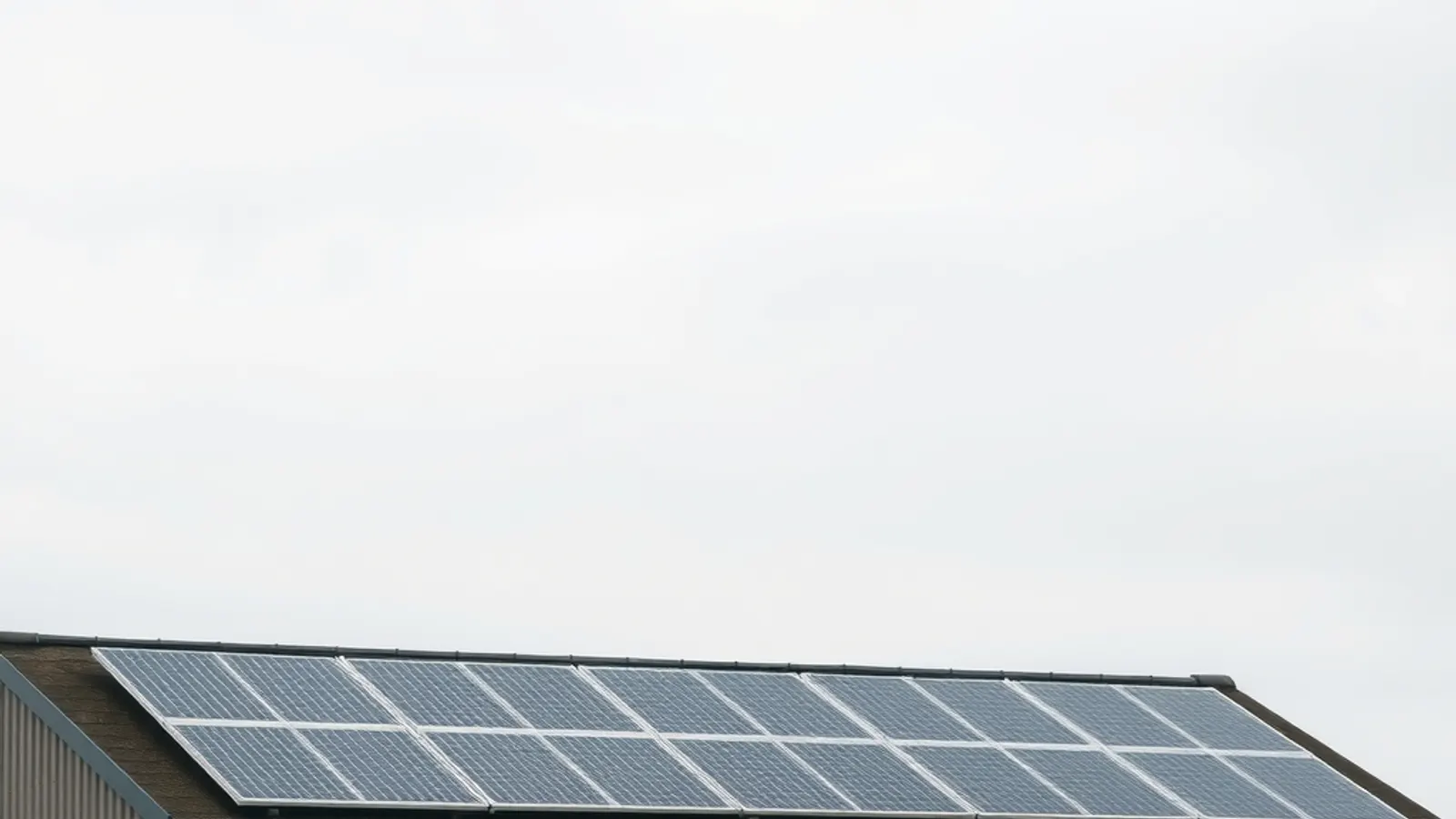 A row of solar panels along the roofline of a UK commercial unit under a soft grey sky